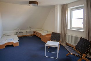 Blick in ein Übernachtungszimmer mit Dachschräge, zwei Betten und einer Sitzgruppe